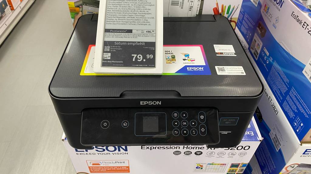 Ein getesteter Drucker unter 100 EUR steht auf der Verpackung mit einem Expression Home EP-3200 von Epson inklusive Preisschild von Saturn.