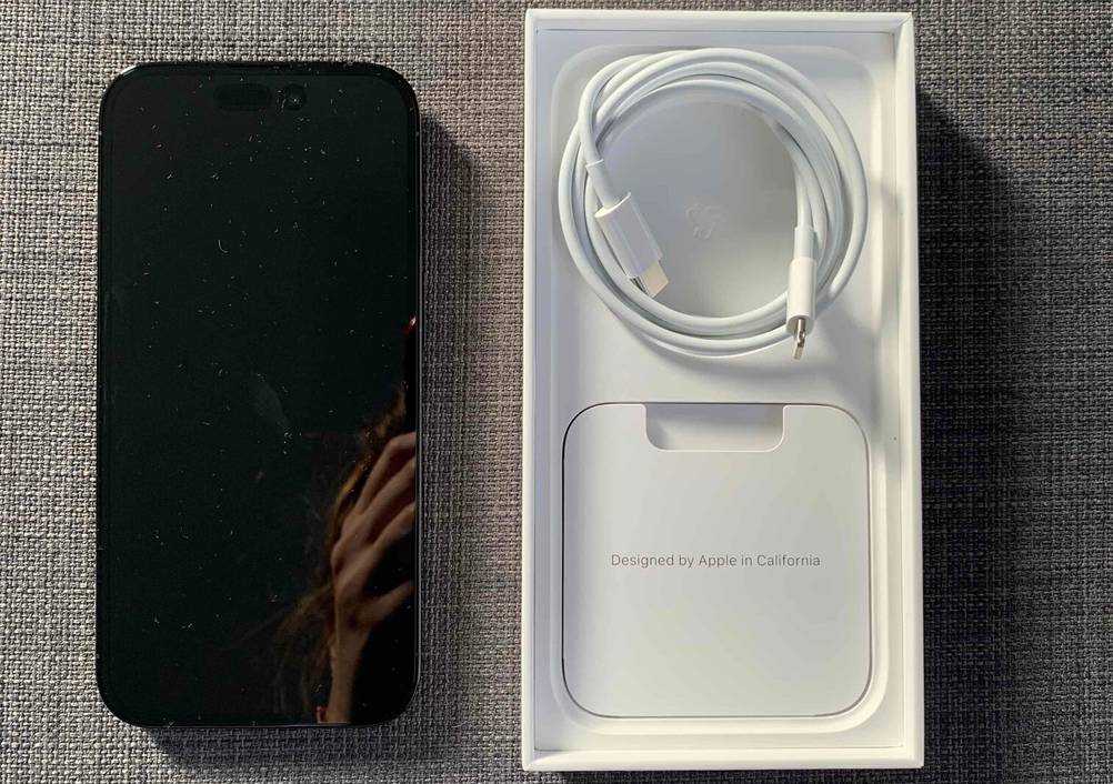 Apple iPhone im Test: Ansicht von oben auf die weiße Apple-Verpackung, die neben einem dunklen Smartphone auf grauem Stoff liegt.