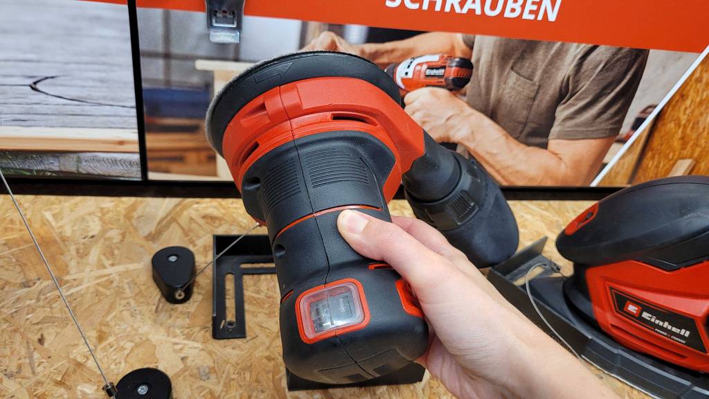 Hand hält einen Akku-Exzenterschleifer über einem Verkaufsregal.