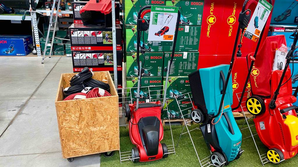 Ansicht des Verkaufsbereichs, indem ein rot-schwarzer Einhell-Elektro-Rasenmäher im Test neben weiteren elektrischen Rasenmähern steht.