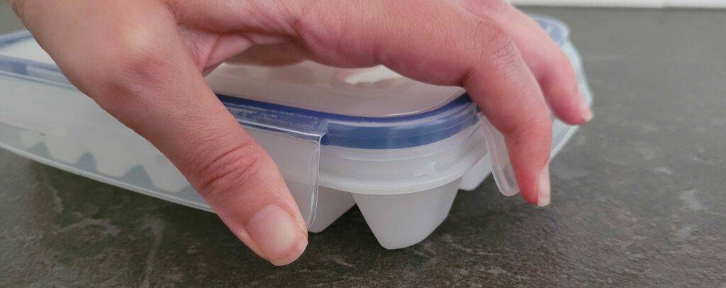Hand schließt den Deckel einer weißen Silikon-Eiswürfelform im Test, die sich auf einer anthrazitfarbenen Oberfläche befindet.