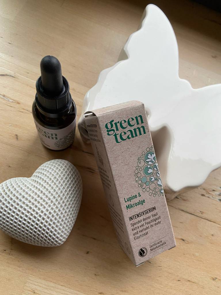 Neben einer weißen Tischdekoration steht eine Verpackung und die braune Flasche mit der getesteten Glättungscreme.