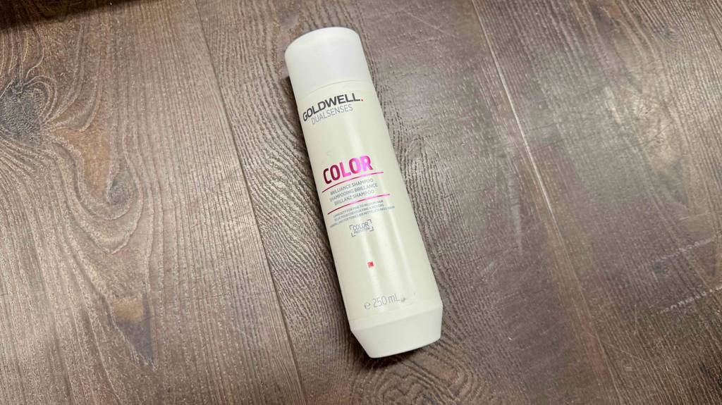 Ein getestetes Goldwell-Shampoo in der weißen Kunststoffflasche liegt auf dem braunen Bodenbelag.