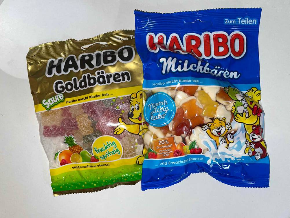 Gummibärchen-Test: Vorderansicht zweier unterschiedlicher Packungen von Haribo, die nebeneinander auf einer weißen Oberfläche liegen.