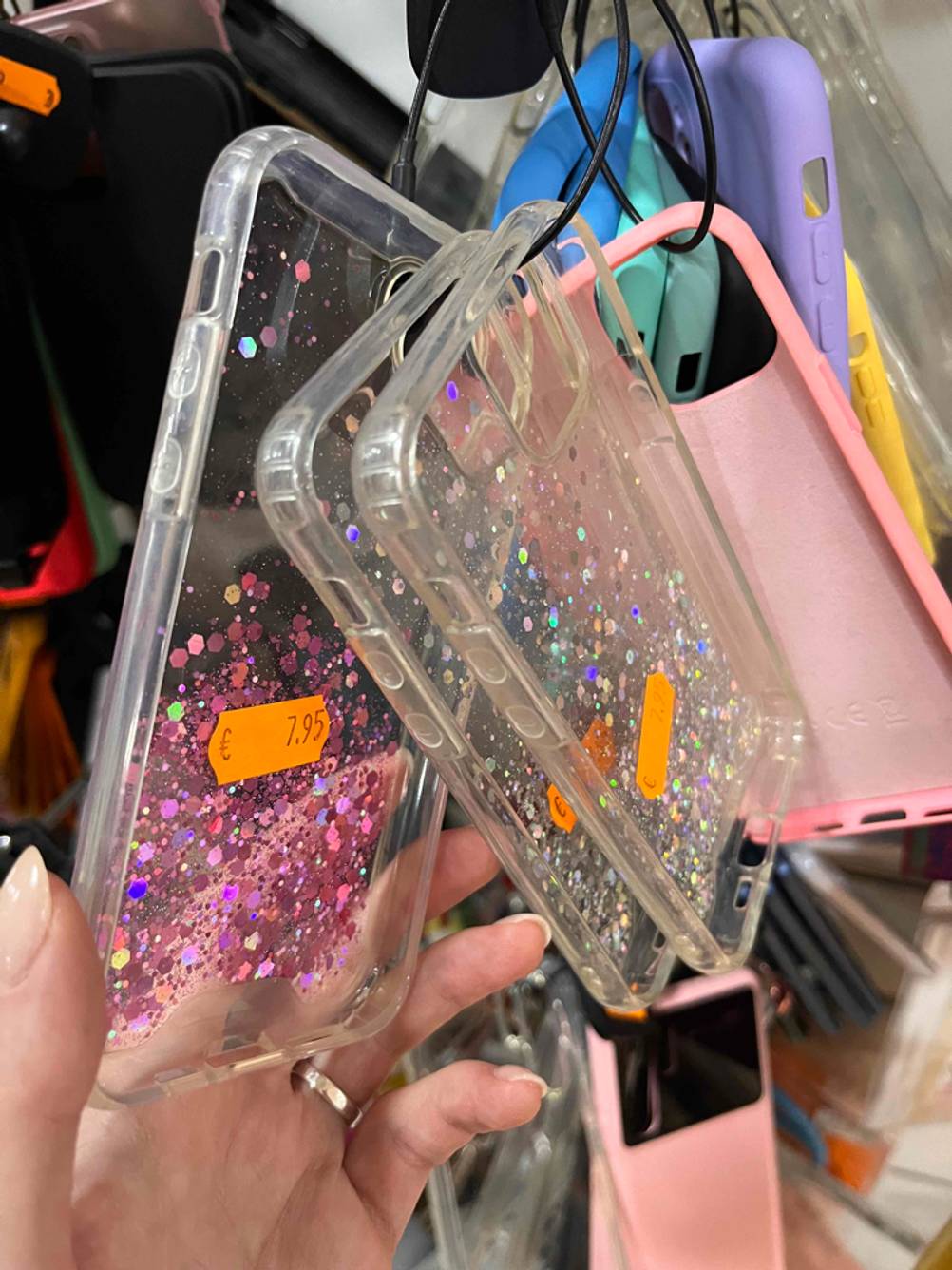 Mehrere getestete iPhone-12-Mini-Hüllen mit Glitzereffekt hängen an einem Verkaufsstand.