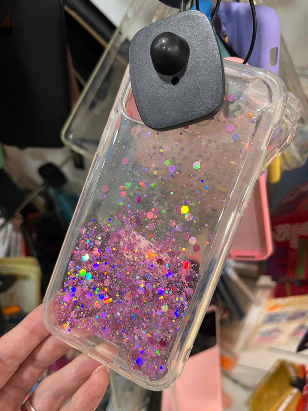 Eine getestete iPhone-12-Mini-Hülle mit Glitzereffekt befindet sich an einem Verkaufsstand.