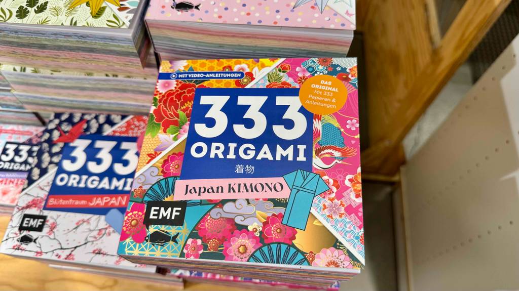 Nahaufnahme von oben auf mehrere gestapelte Bücher inklusive der 333 unterschiedlicher, getesteter Origami-Papiere.