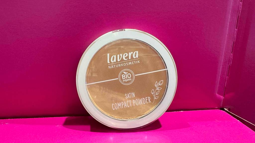 Das getestete Naturkosmetik-Make-up in der Dose mit transparentem Deckel steht in einem pinkfarbenen Karton.