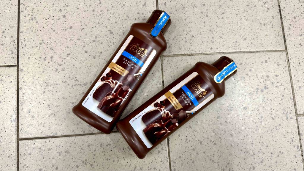 Kuchenglasur Test: Zwei braune Quetschflaschen mit Glasur von Lindt liegen auf einem Fliesenbelag.