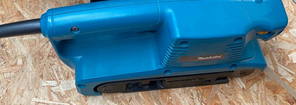 Ansicht von oben auf einen blauen Makita-Bandschleifer im Test, mit Fokus auf die Schleifbandführung bis zur Gehäusekante.