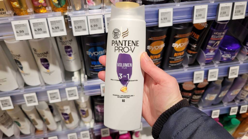 Eine Hand hält eine Quetschflasche mit Pantene-Pro-V-Shampoo im Test vor einem Drogeriemarktregal.