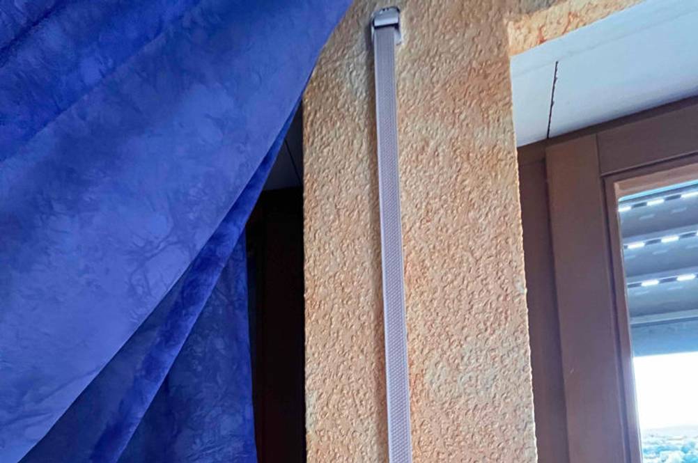 Weißer langer Rollladengurt im Test zwischen Fenster und blauem Vorhang auf oranger Wand.