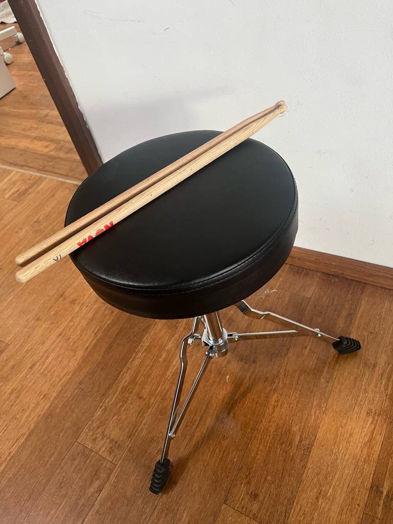 Auf einem Schlagzeug-Hocker im Test liegen zwei Schlagzeugstäbe aus Holz.