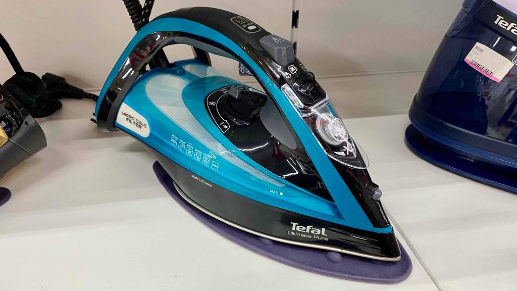 Im Test: ein Bügeleisen von Tefal in türkis-schwarz steht auf einem weißen Verkaufsregal zwischen anderen Dampf-Bügeleisen.