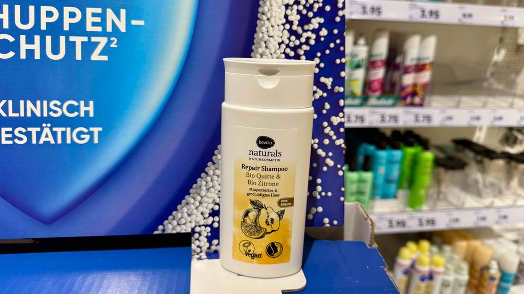 Ein getestetes veganes Shampoo von Bevola steht auf einem Karton vor dem Regal mit Kosmetikartikeln.