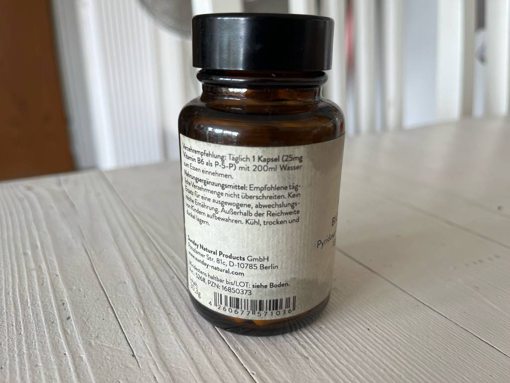 Vitamin-B6 im Test: eine blickdichte Glasdose mit Drehverschluss und weißem Etikett inklusive Verzehrempfehlung steht auf einer weißen Holzfläche.