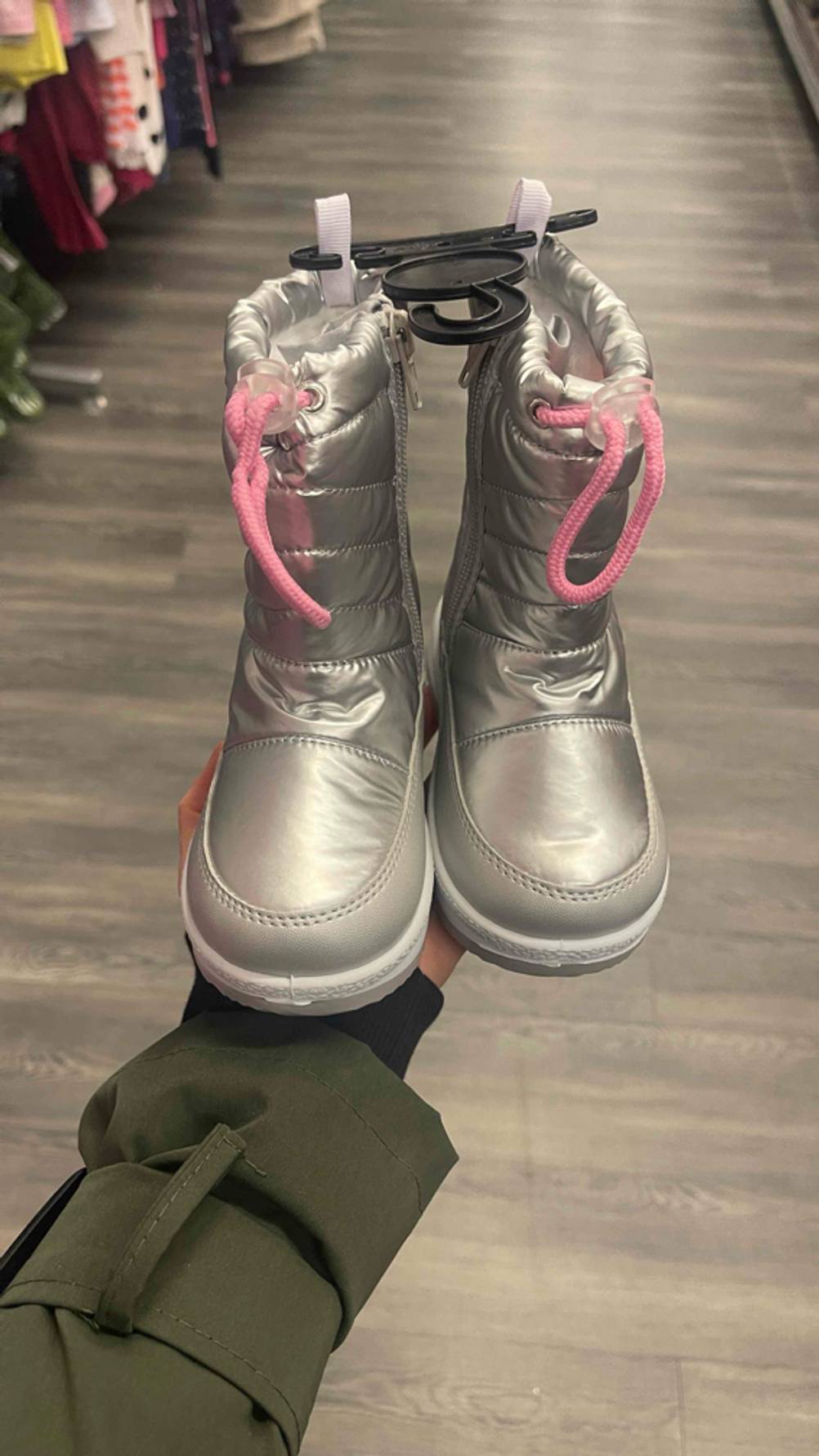 Getestet: Die silberfarbenen, getesteten Winterstiefel für Kleinkinder stehen auf einer Handfläche neben einem Verkaufsregal.
