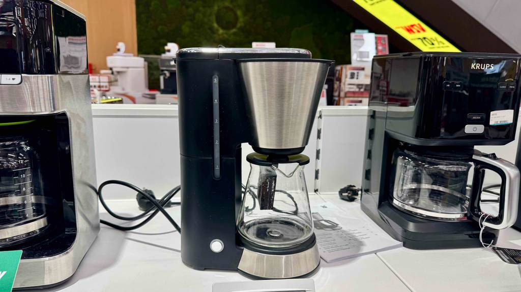 Eine getestete WMF-Kaffeemaschine steht zwischen zwei Kaffeemaschinen auf einem Ausstellungsregal.