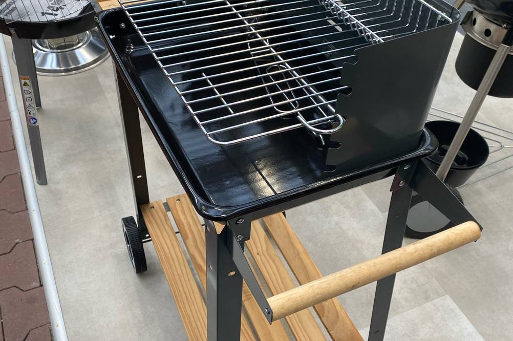 Gesamtansicht eines fahrbaren Grillwagens im Test: schwarzes Modell inklusive zwei höhenverstellbarer Grillflächen sowie zwei Holzablagen im unteren und seitlichen Bereich des Gestells.