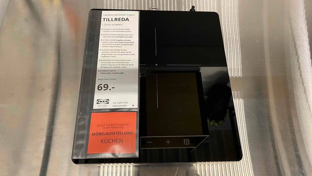 Tragbares, schwarzes, getestetes Induktionskochfeld Tillreda von Ikea steht inklusive Preisschild auf hellem Untergrund.
