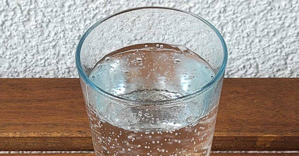 Detailansicht eines transparenten Trinkglases mit getestetem Adelholzener Wasser mit natürlicher Kohlensäure von oben betrachtet.