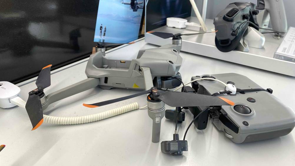 Seitenansicht auf eine im Verkauf ausgestellte DJI-Drohne im Test: Das hellgraue Kamera-Drohne ist neben seiner Fernsteuerung platziert.