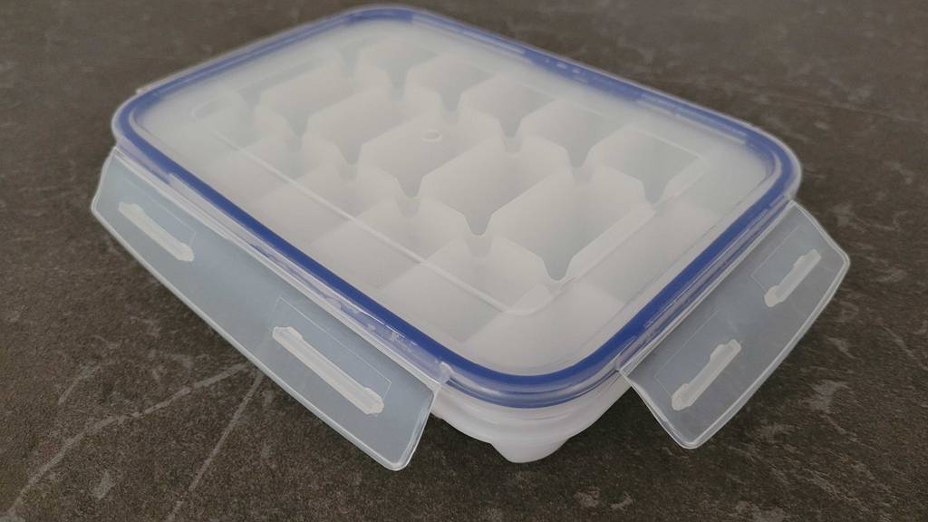 Getestet: Eine weiße Eiswürfelform für rechteckige Eiswürfel steht inklusive Deckel und blauer auslaufsicherer Dichtung auf einem anthrazitfarbenen Untergrund.