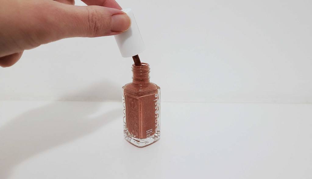 Getesteter Essie-Nagelack in einer Flasche, über der eine Damenhand den Pinsel am Schraubverschluss hält.