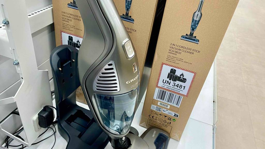 Seitliche Detailansicht des transparenten Staubfangbehälters eines Grundig-Akku-Staubsaugers im Test inklusive schwarzer Ladestation vor dem braunen Originalkarton.