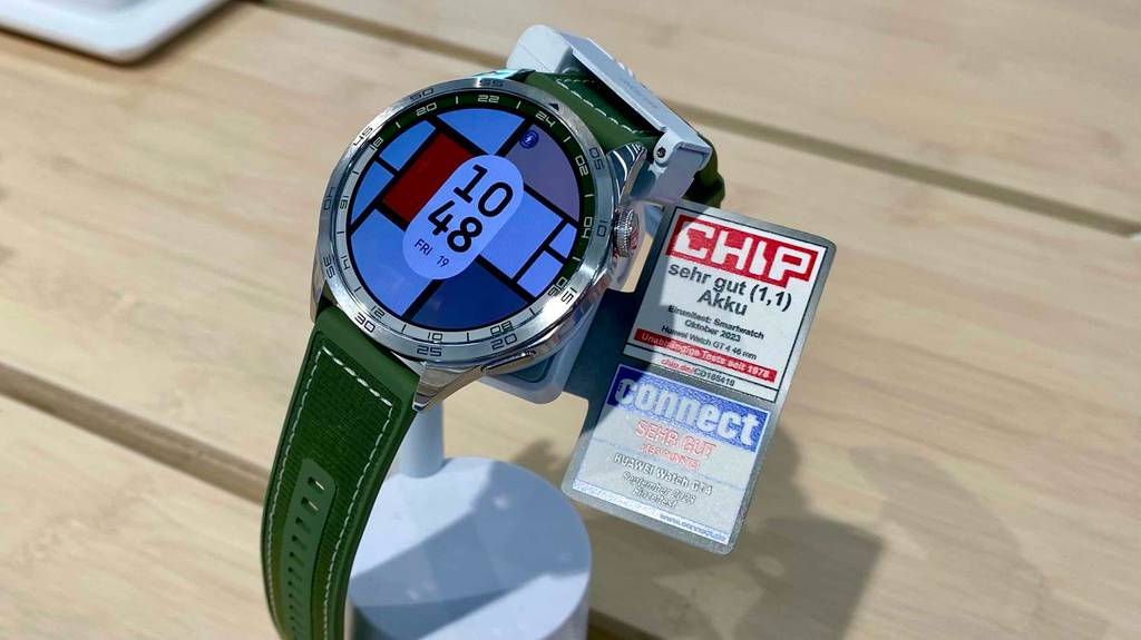 Nahaufnahme einer eingeschalteten Huawei-Smartwatch im Test inklusive Uhrzeit und Datum auf einem runden Bildschirm inklusive Metallrahmen und grünem Armband.