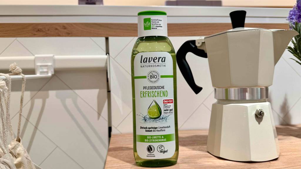 Eine transparente Quetschflasche mit Lavera-Duschgel im Test steht auf einem Regal neben einem italienischen Kaffeekocher im Verkaufsbereich.