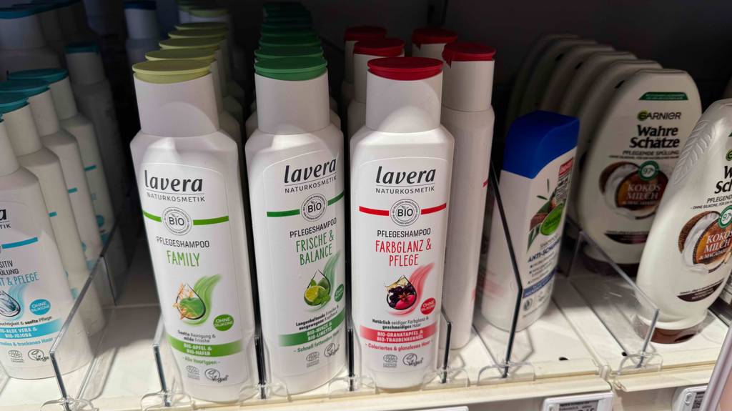 Mehrere weiße Kunststoffflaschen mit getestetem Lavera-Shampoo stehen auf einem Regal im Drogeriemarkt.
