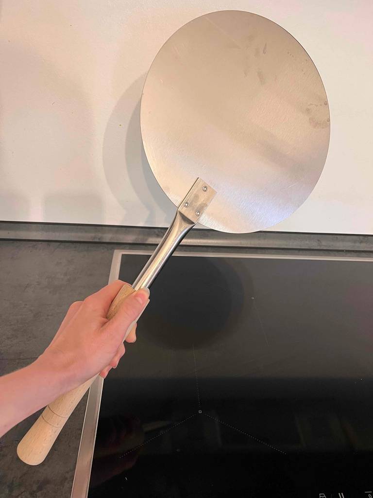 Eine Hand hält eine Pizzaschaufel im Test über einer Herdplatte.