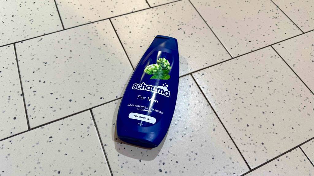 Eine blaue Quetschflasche mit getestetem Schauma-Shampoo für Männer liegt auf einem Fliesenboden.