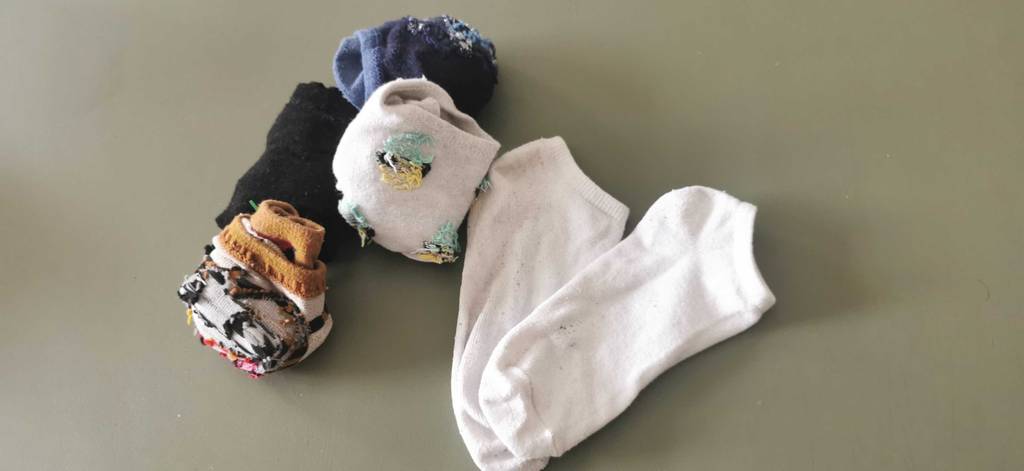 Eingerollte und getestete Sneaker-Socken liegen neben einem ausgebreiteten weißen Paar Socken auf einer olivgrünen Oberfläche.