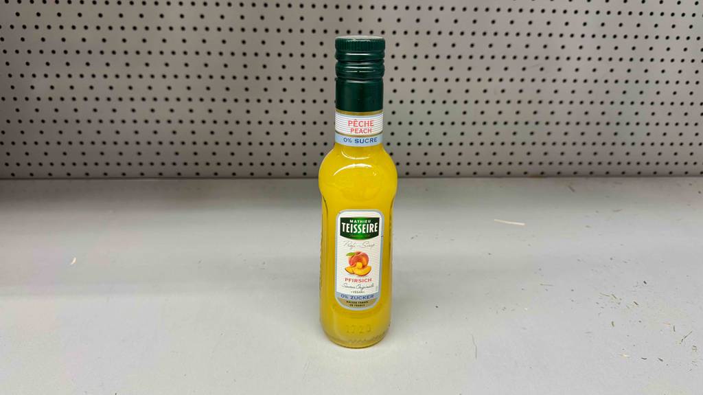 Eine Flasche mit getestetem Teisseire-Sirup in Pfirsich-Geschmack steht vor einem weißen Untergrund.