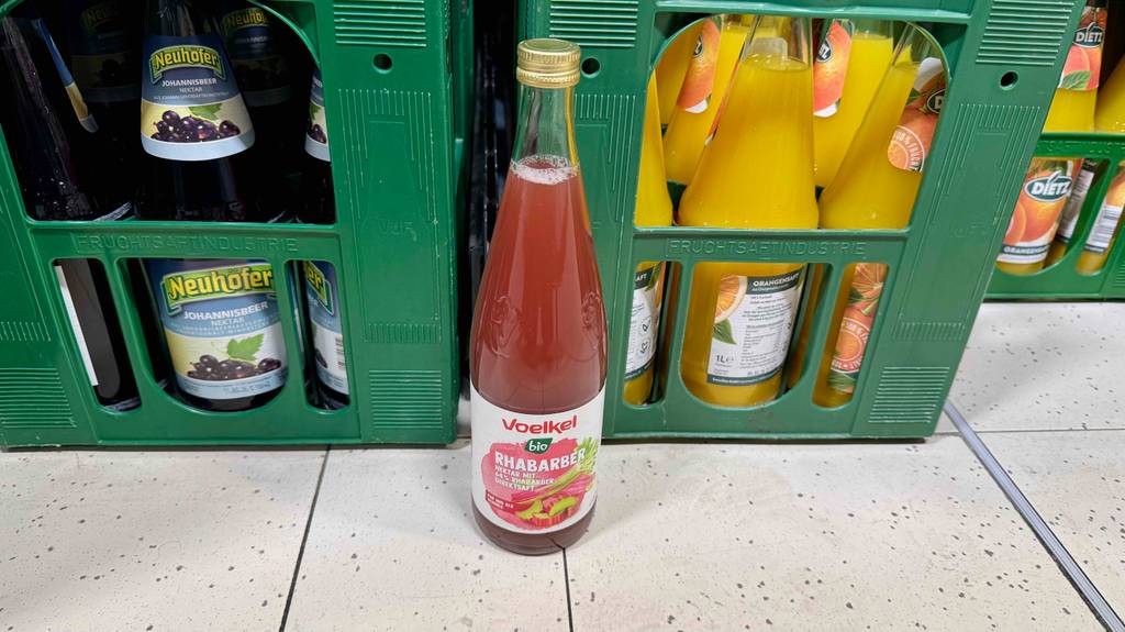 Eine Glasflasche mit getestetem Voelkel-Saft steht auf dem Boden vor Flaschenkästen im Supermarkt.