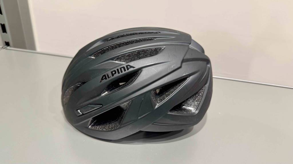 Der schwarze Alpina-Fahrradhelm im Test liegt auf einer weißen Oberfläche.