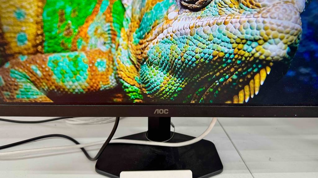 Detailansicht des getesteten AOC-Gaming-Monitors inklusive Standfuß, dermit hochauflösendem Bildschirm auf einem Ausstellungsregal steht.