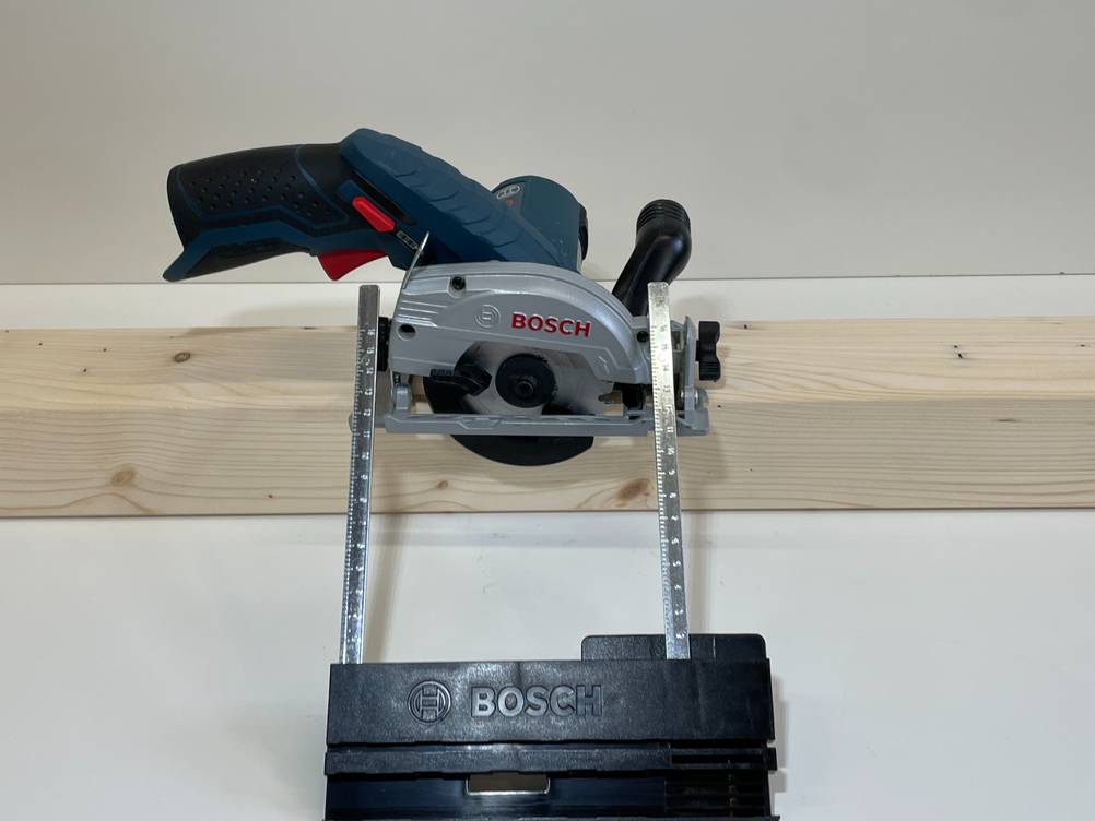 Auf einem Stück Holz befindet sich eine getestete Bosch-Handkreissäge inklusive Messvorrichtung.