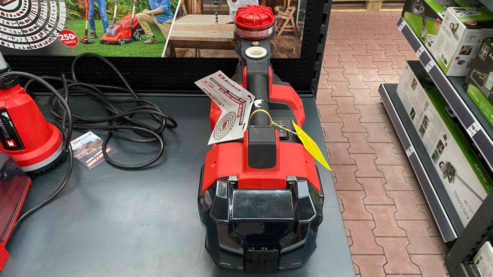 Draufsicht Einhell-Gartenpumpe-Test: eine rote Einhell-Gartenpumpe Aquina steht mit anderen Gartenutensilien auf einem Podest.