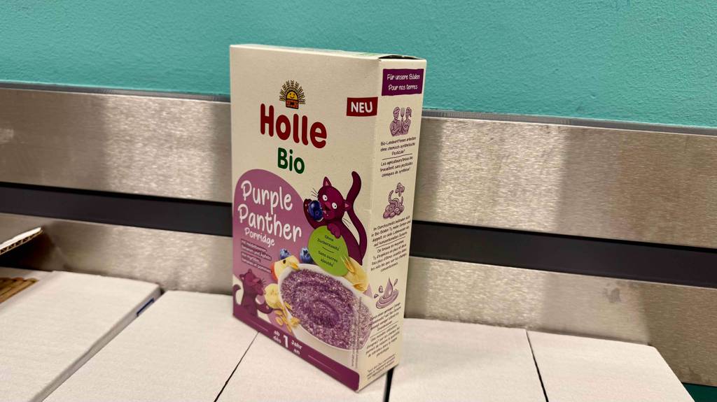 Die getestete Holle-Babynahrung in der Verpackung mit Gebrauchsanleitung steht auf Kartons in einem Verkaufsregal.