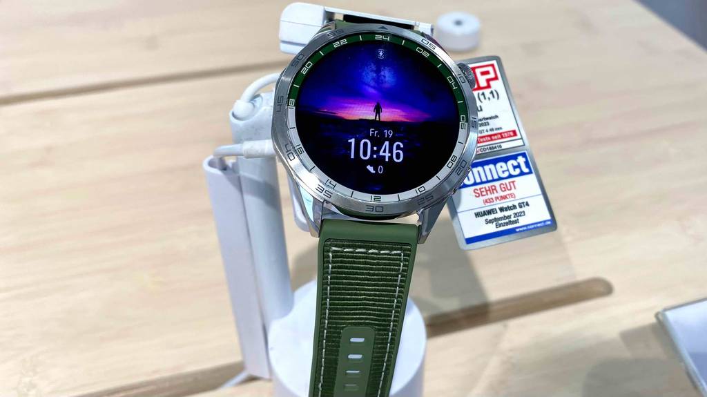 Nahaufnahme einer eingeschalteten getesteten Huawei-Smartwatch mit rundem Bildschirm inklusive Metallrahmen und Uhrzeit grünem Armband.