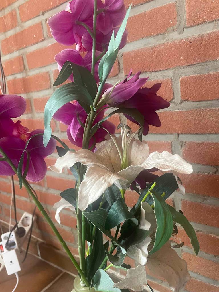 Vor einer Ziegelwand steht eine Vase mit roten und weißen Kunstblumen im Test.
