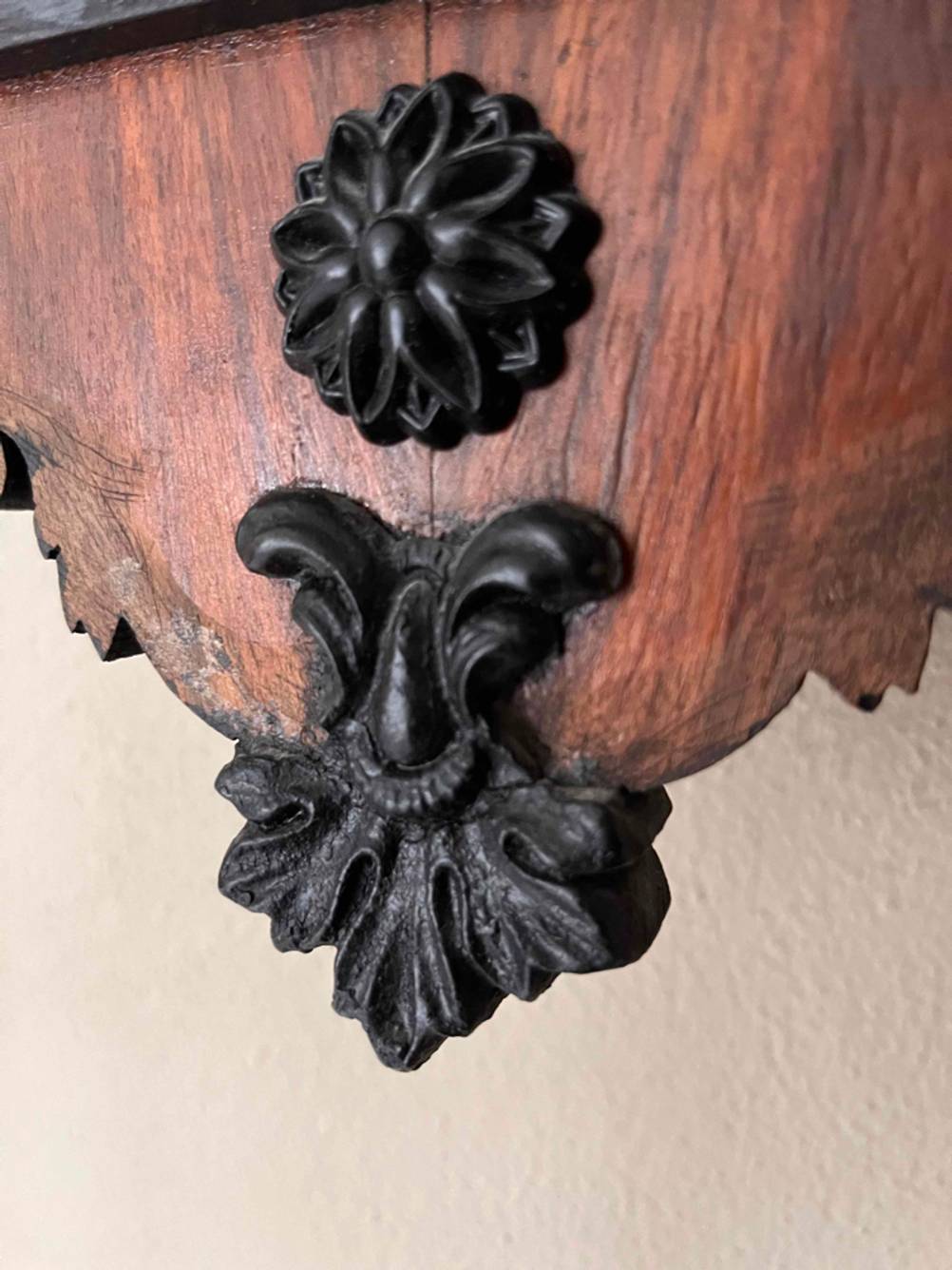Detailaufnahme der geschnitzten Verzierung am unteren Eck einer Holz-Pendeluhr im Test.