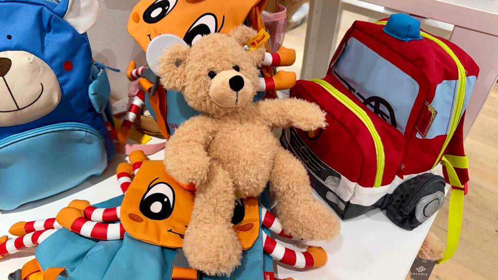 Der getestete Steiff-Teddy sitzt auf mehreren Kinder-Rucksäcken im Geschäft.