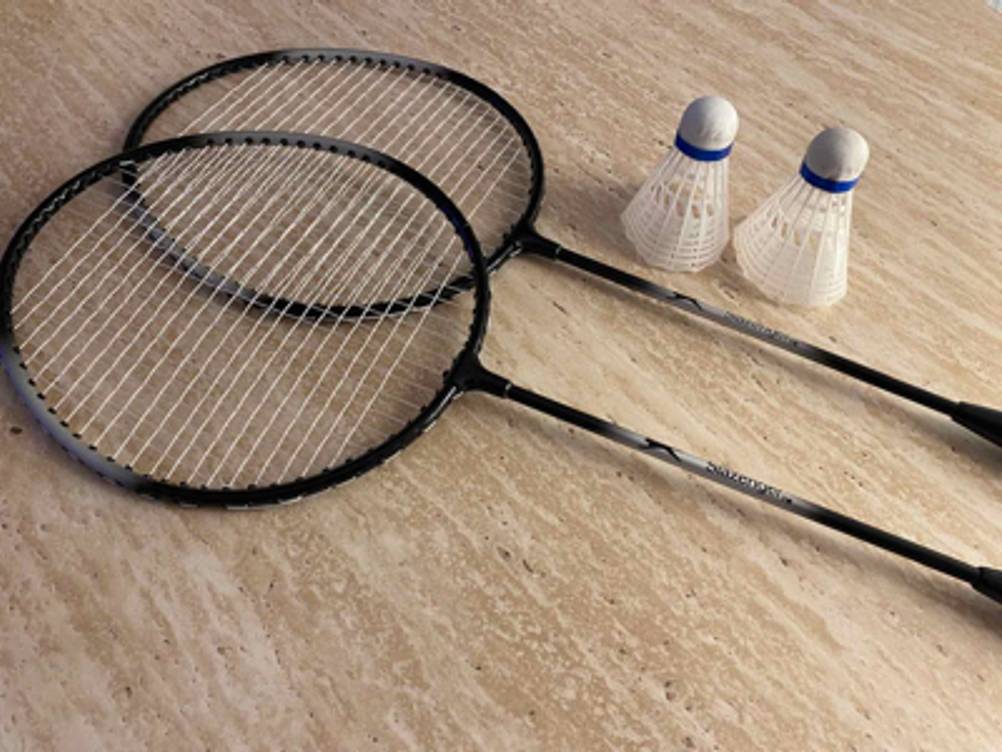 Federball-Sets im Test: Zwei schwarze Ferballschläger und zwei Federbälle liegen nebeneinander auf einer beigefarbenen Oberfläche.