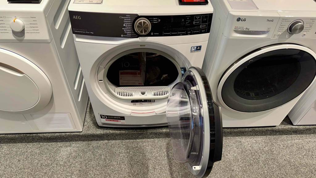AEG-Trockner im Test: Das Modell befindet sich mit geöffneter Rechtsanschlag-Tür zwischen weiteren Trocknern auf einer Ausstellungsfläche im Verkauf.