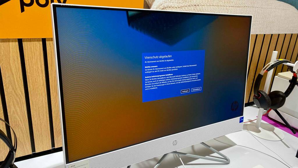 Weißer getesteter All-in-One-PC mit eingeschaltetem Bildschirm inklusive Virenschutz-Abgelaufen-Benachrichtigung, neben einem schwarzen Over-Ear-Kopfhörer.