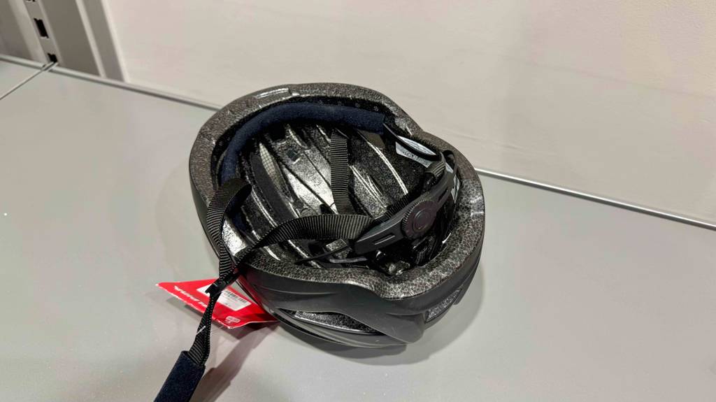 Der getestete Alpina-Fahrradhelm in Schwarz liegt, mit Fokus auf das Innere, auf einem weißen Regal.